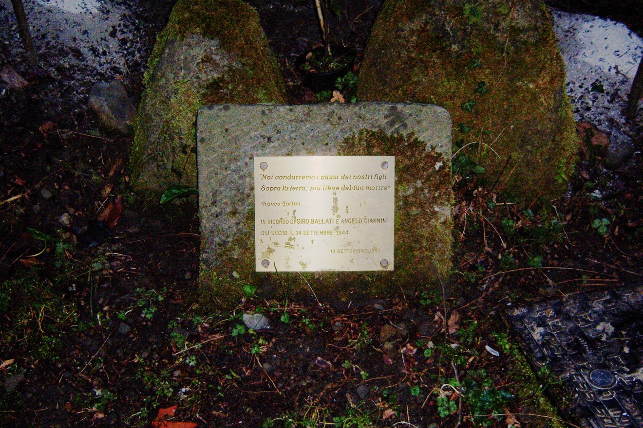 Cippo commemorativo dedicato a Ballati e Giannini, immerso nella vegetazione.