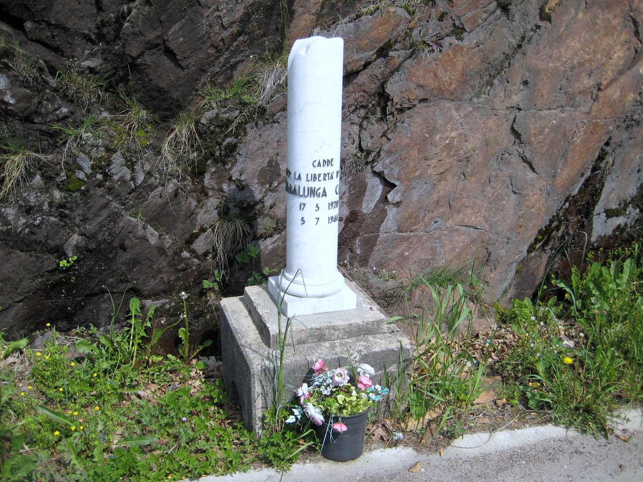 Cippo commemorativo a Gambalunga, con fiori e roccia sullo sfondo. Symbolo di memoria e ricordo.