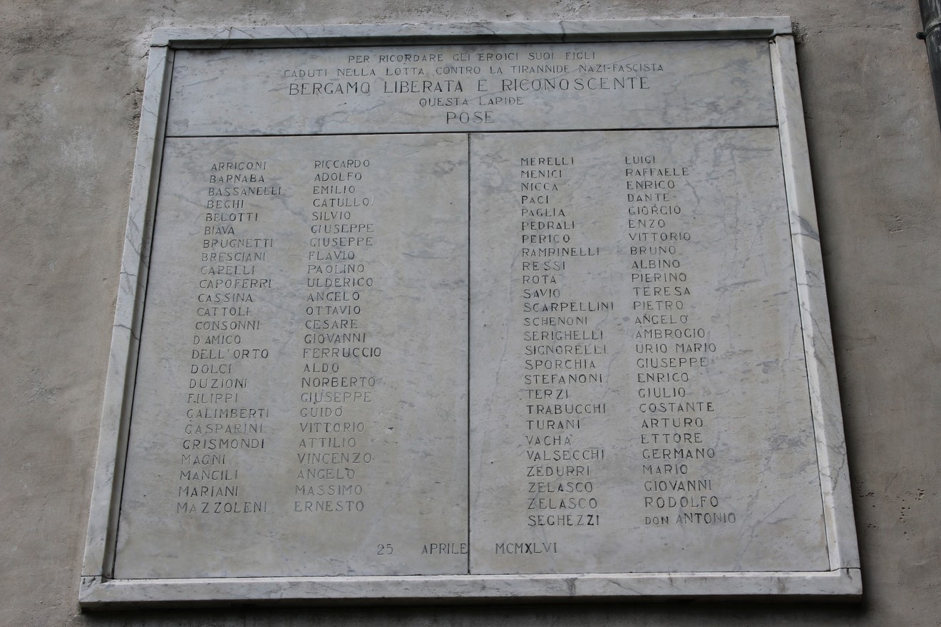 Stele commemorativa dedicata ai partigiani caduti, con nomi incisi in marmo su fondo chiaro.
