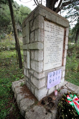 Monumento commemorativo dedicato alla strage di Piedipaterno, immerso nella natura con una corona di fiori.