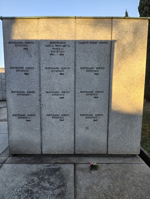 Monumento commemorativo con iscrizioni dedicate ai partigiani e ai caduti, illuminato dalla luce del sole.