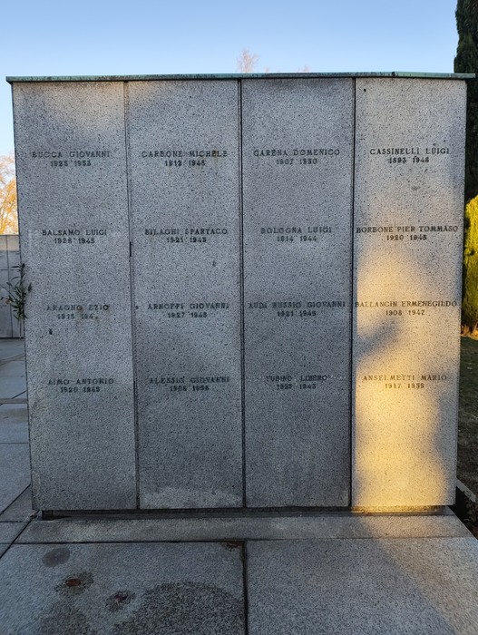 Monumento commemorativo con nomi incisi, dedicato ai caduti, immerso in un contesto di natura.