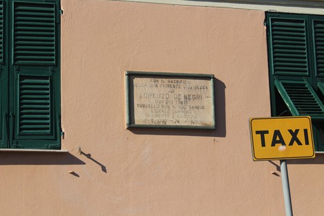 Lapide commemorativa di Lorenzo De Negri su una parete, accanto a un'insegna taxi.