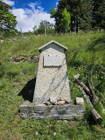 Cippo commemorativo in pietra, circondato da vegetazione e rocce, in un'area naturale a Casel.
