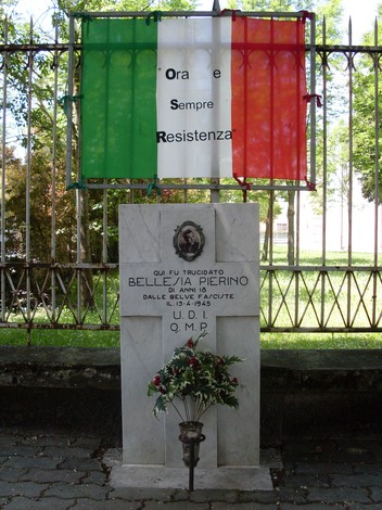 Cippo commemorativo a Bellesia, in onore della Resistenza, con decorazioni e fiori.