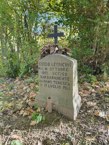 Cippo commemorativo di Guido Leoncini, martire della guerra, con croce e decorazioni naturali.