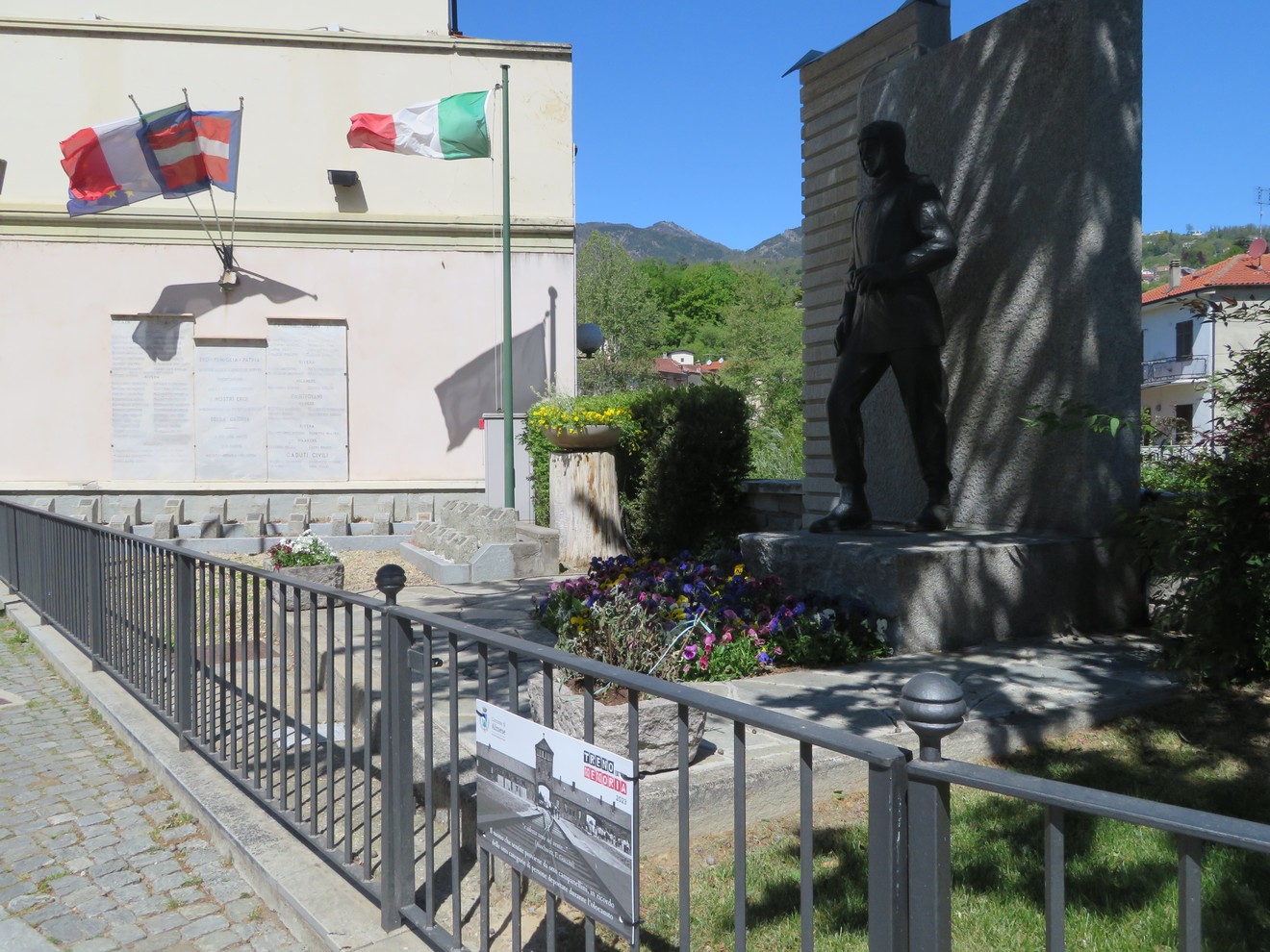 Lapide commemorativa ai caduti di Almese, con statue e decorazioni floreali in un contesto suggestivo.