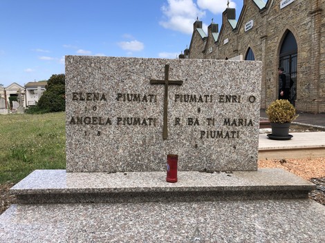 Sepolcro di Piumini, con croce e candele, situato in un cimitero storico.