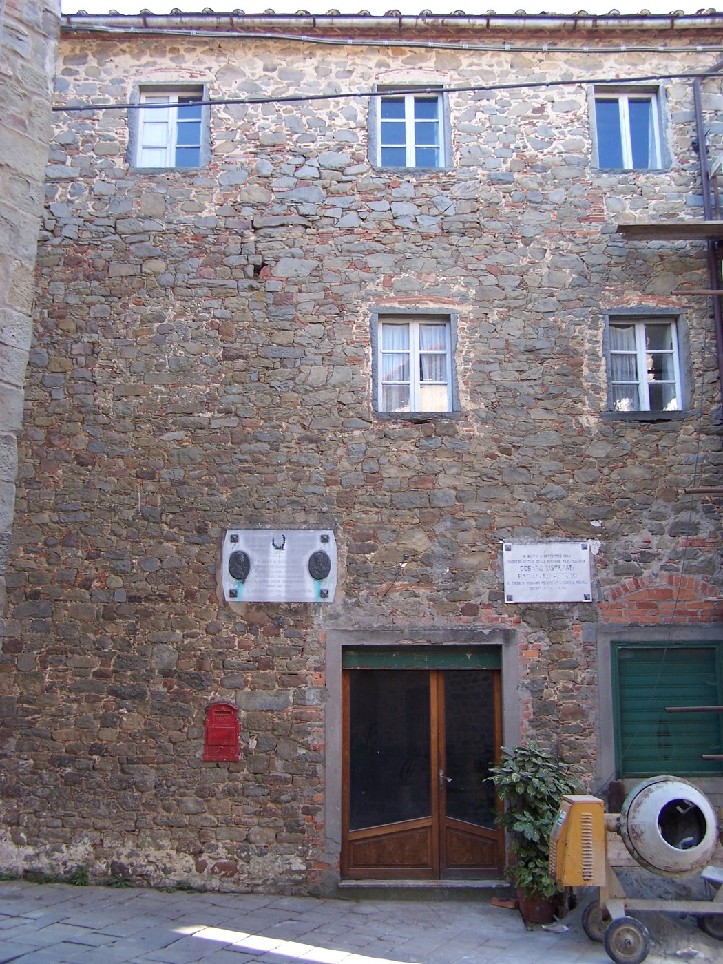 Lapide commemorativa su una facciata di edificio in pietra, con dettagli architettonici tipici.