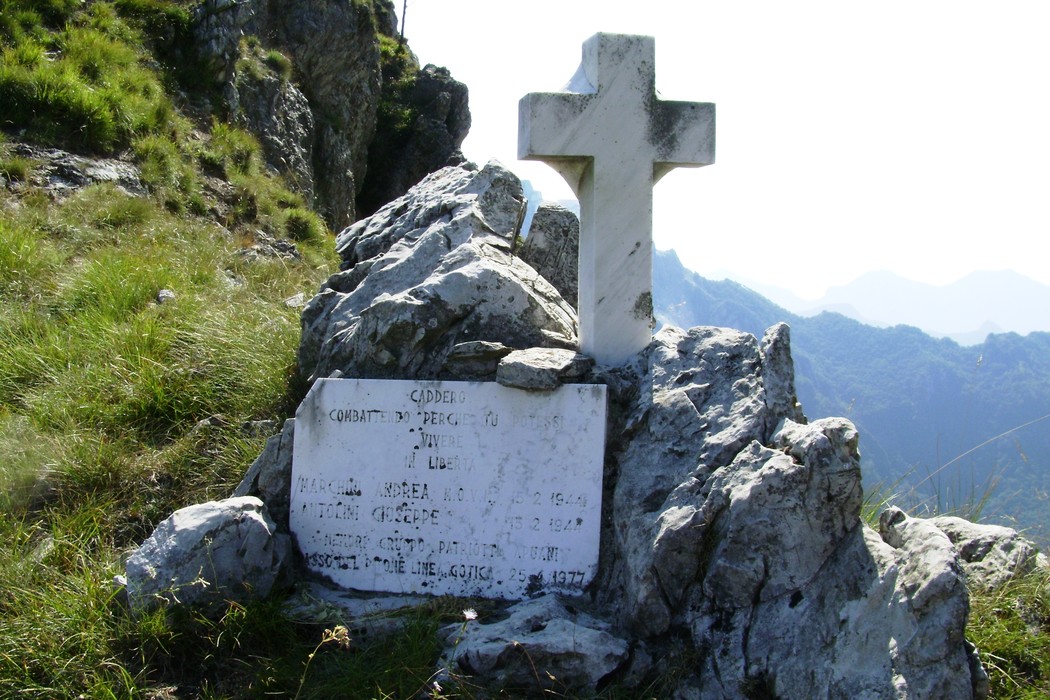 Cippo commemorativo dedicato a Marchini e Antolini, situato in un paesaggio montano.