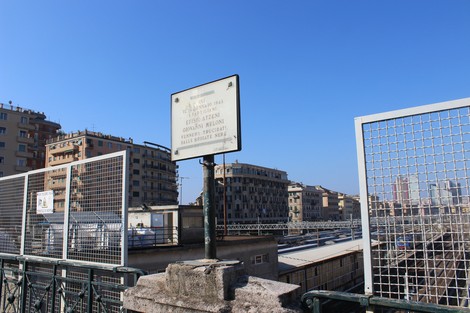 Lapide commemorativa dedicata a Atzeni e Meloni, visibile in un contesto urbano. Sullo sfondo si intravedono edifici e cielo blu.