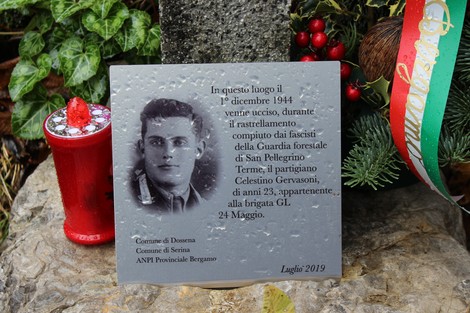 Croce commemorativa dedicata a Celestino Gervasoni, partigiano ucciso nel 1944, circondata da fiori e oggetti decorativi.