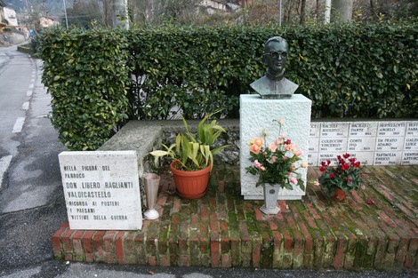 Monumento dedicato a Don Raglianti, con busto, fiori e dedica commemorativa in un contesto verde.