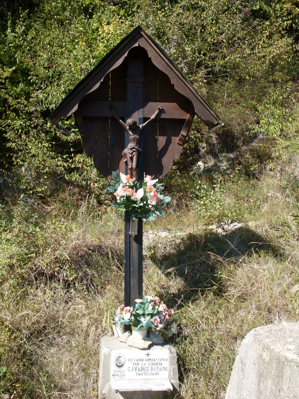 Croce a Busani, simbolo di fede immerso nella natura, decorata con fiori e un Cristo crocifisso.