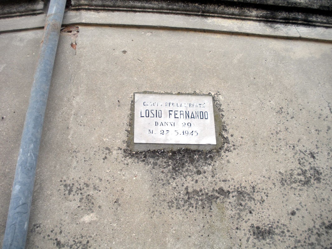 Lapide commemorativa dedicata a Losio Fernando, situata su una parete esterna.