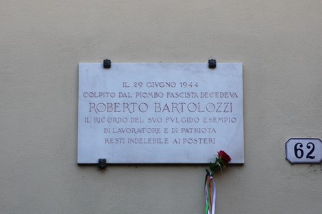 Lapide commemorativa a Bartolozzi, vittima del fascismo, con un omaggio floreale.