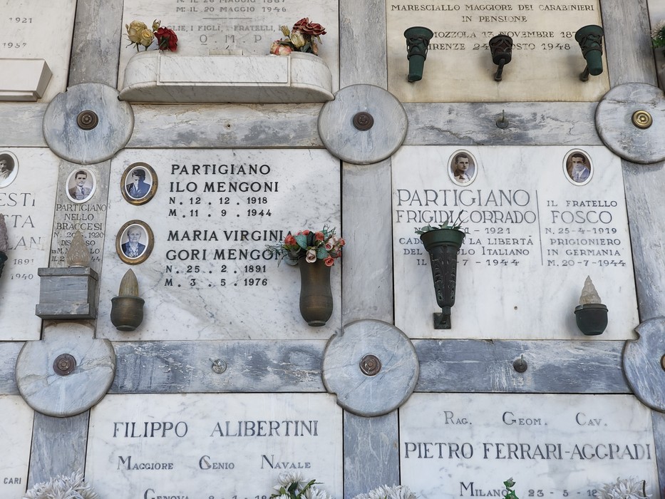 Loculi cimiteriali in marmo con lapidi e iscrizioni, decorati con fiori, foto e piccoli oggetti commemorativi.