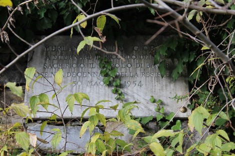 Lapide in pietra circondata da vegetazione, dedicata a Merlanti, con iscrizioni storiche.