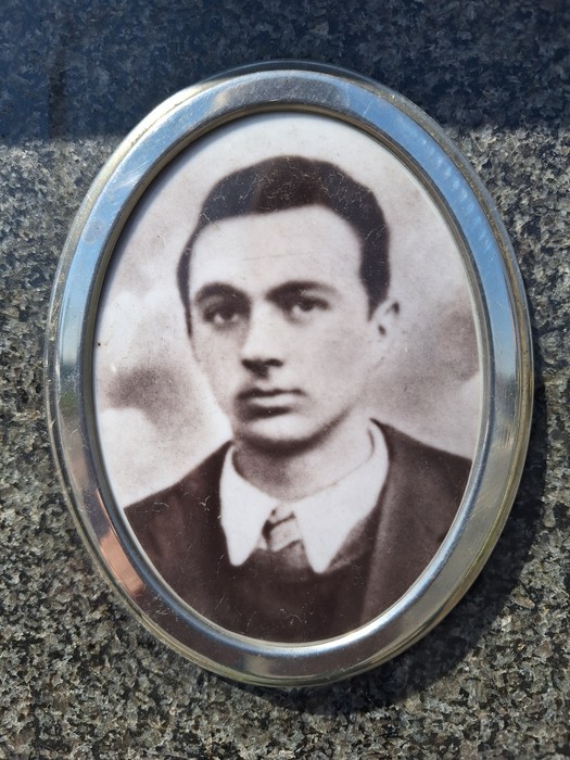 Ritratto in bianco e nero di un giovane uomo, inserito in una cornice ovale, su uno sfondo scuro.