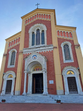 Facciata di una chiesa con mattoni rossi, finestre ornate e un grande portico, illuminata da luce naturale.
