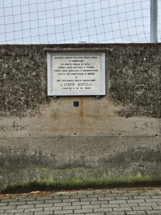 Lapide commemorativa dedicata a Sergio Bertelli, situata su un muretto in un contesto esterno.