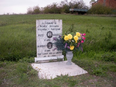 Lapide commemorativa dei partigiani Pizzi e Alberici, con fiori, in un'area verde.