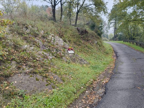 Targa commemorativa su un masso lungo un sentiero immerso nella natura. Atmosfera mistica e silenziosa.