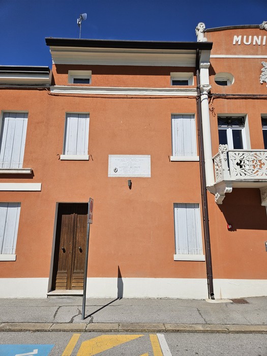 Lapide dedicata a Beltrame su un edificio di colore arancione con finestre bianche.