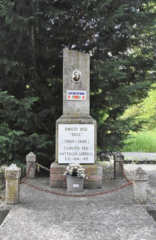 Cippo commemorativo dedicato a Emilio Bigi, caduto per l'unità libera, immerso nel verde circostante.