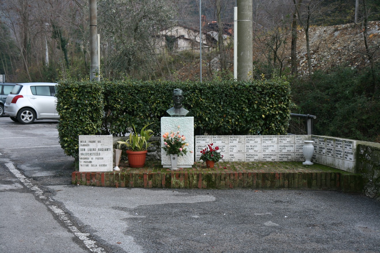 Monumento a Don Raglianti, commemorazione con busto e dedica in un'area curata tra piante e fiori.