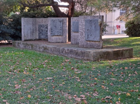 Monumento ai Caduti, composto da lastre commemorative su una base di pietra, circondato da vegetazione e foglie secche.