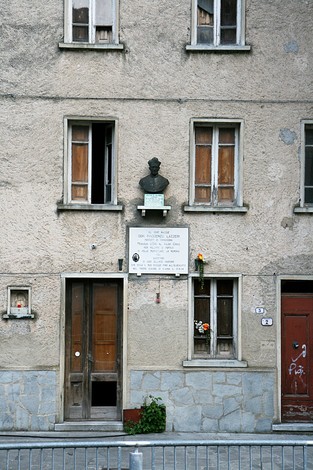 Lapide commemorativa e busto di Don Lazzeri su una facciata di edificio storico.