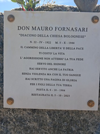 Cippo commemorativo dedicato a Don Mauro Fornasari, con iscrizioni che celebrano il suo servizio e i valori di libertà e pace.