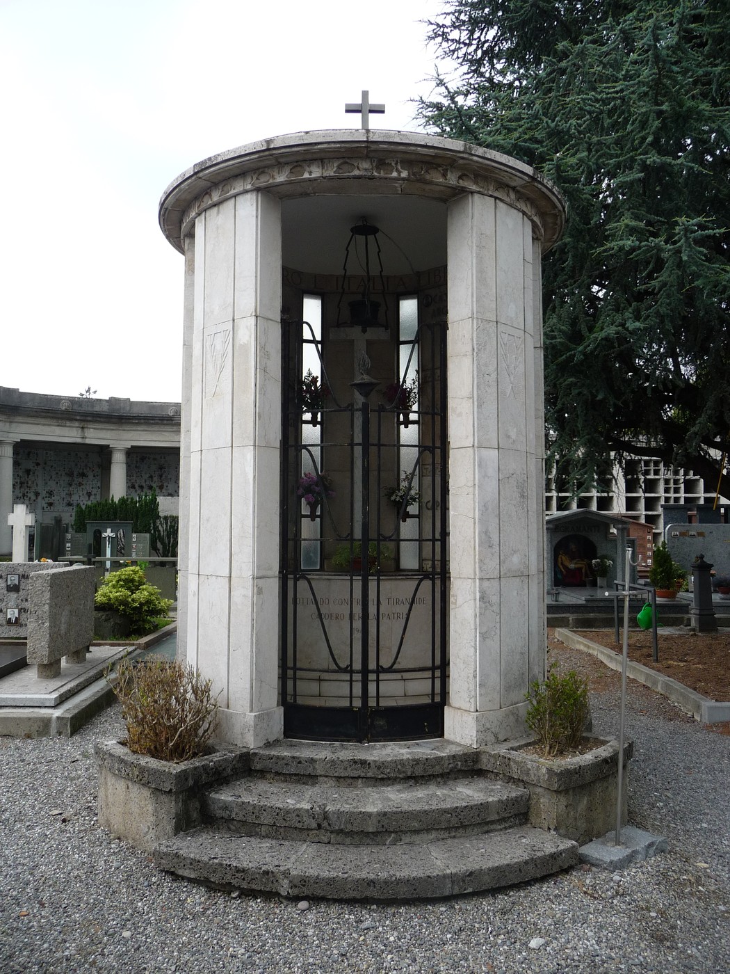 Monumento in stile architettonico elegante, dedicato ai caduti partigiani, circondato da lapidi e vegetazione.