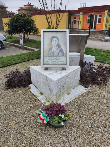 Monumento a Degli Esposti con ritratto e decorazioni floreali in un contesto urbano.