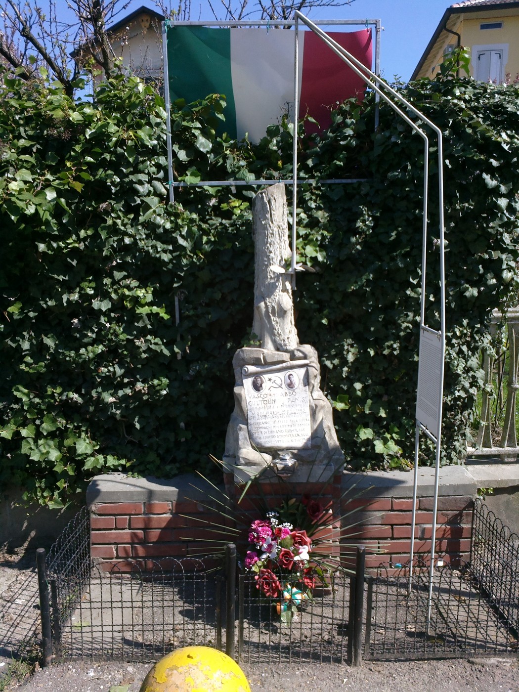 Cippo commemorativo dedicato a Guaitolini e Panisi, decorato con un tricolore italiano e fiori.