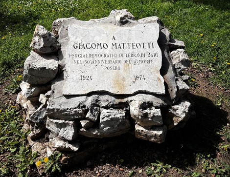 Cippo commemorativo dedicato a Giacomo Matteotti, con iscrizione sulla pietra, circondato da un prato verde.