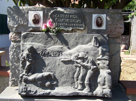 Cippo commemorativo dedicato a Caprai e Creatini, adornato da fiori e immagini in un contesto storico.
