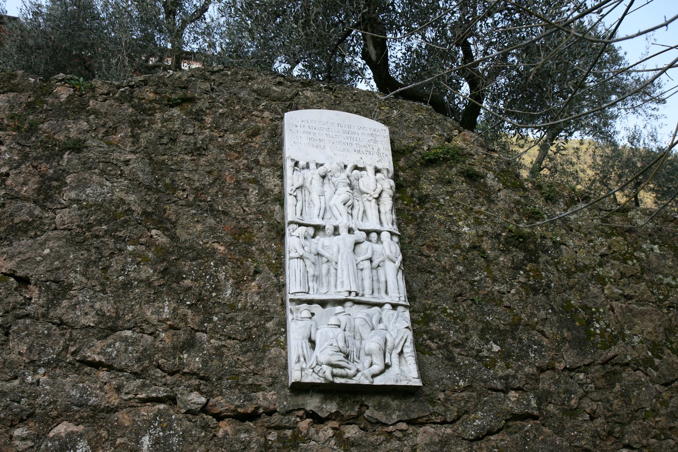Lapide in memoria dei caduti di Valdicastello, incastonata in una roccia circondata da olivi.