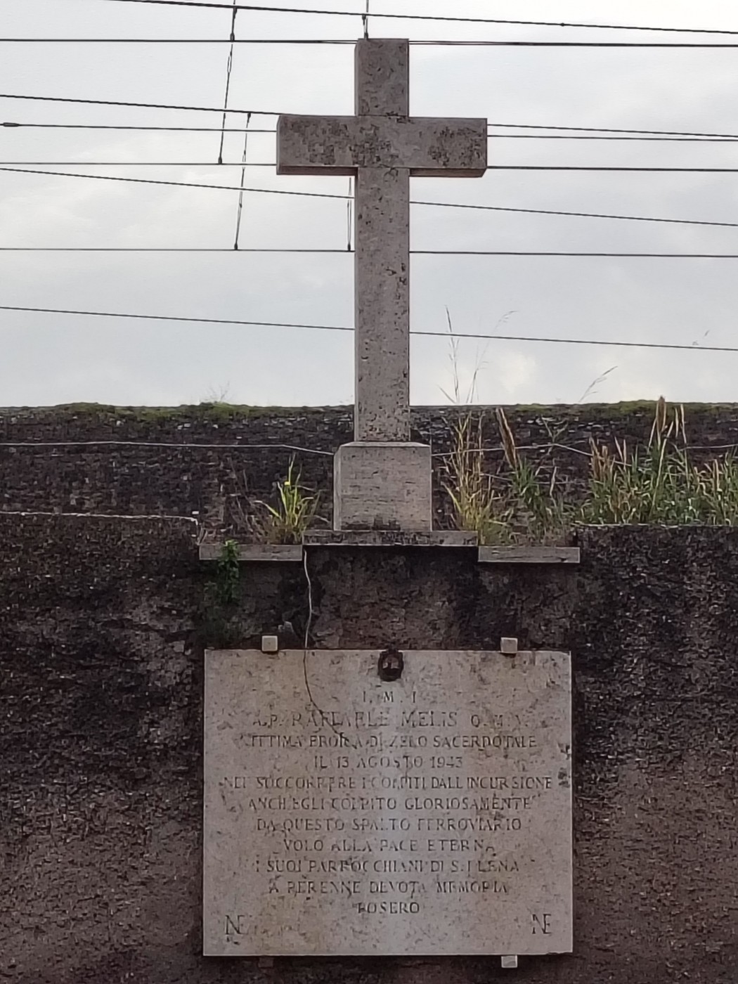 Croce a Melis, monumento religioso con iscrizione dedicatoria, immersa in un ambiente naturale.