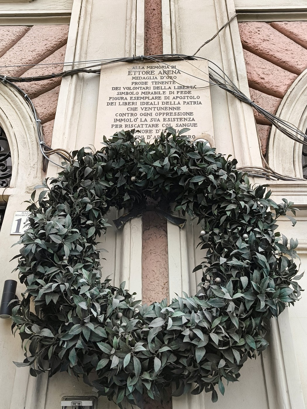 Lapide commemorativa con una corona di foglie verdi, situata su una parete in città.