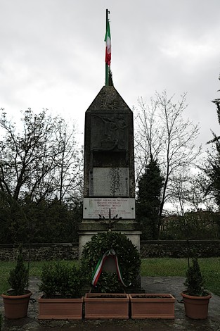 Obelisco commemorativo ai caduti di San Piero a Sieve, circondato da piante e decorato con il tricolore italiano.