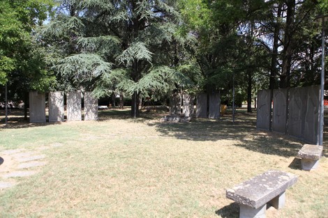 Monumento ai Martiri del Panaro circondato da alberi e spazi verdi, con pannelli commemorativi in pietra.