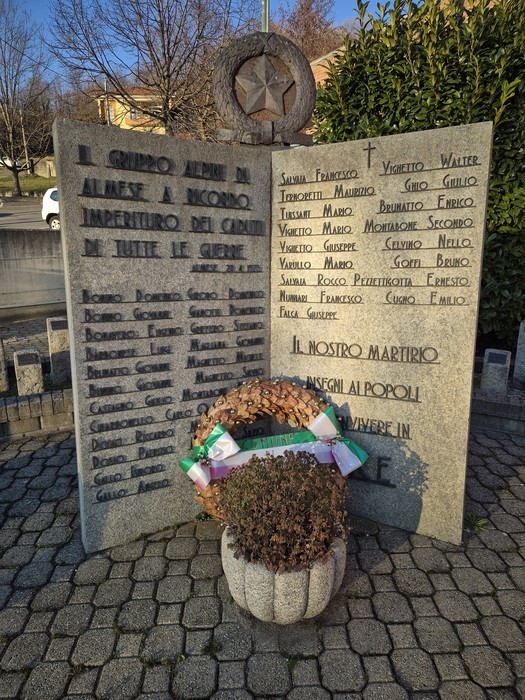 Monumento in pietra con stella e croce, elenco di nomi inciso, corona di pigne alla base.