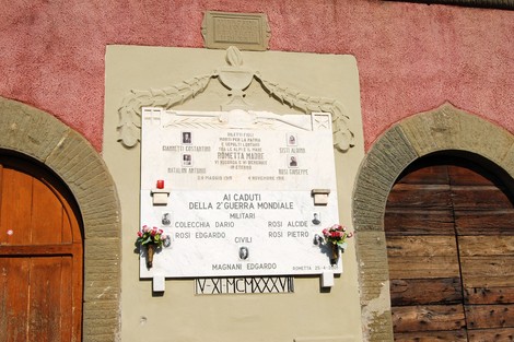Lapide commemorativa ai caduti della Seconda Guerra Mondiale a Rometta, decorata con fiori e incisi ricordi.