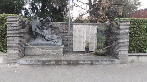 Monumento commemorativo ai caduti con sculture e elenco di nomi incisi, immerso nel verde di Cavenago.