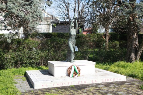 Monumento alla 63° Brigata Garibaldi, con statua centrale e corona d'alloro, immerso nel verde circostante.