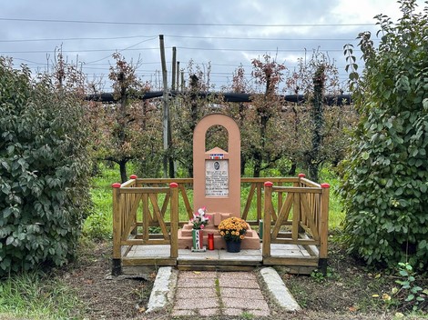 Cippo commemorativo a Guaitoli, immerso nel verde, tra piante e fiori, dedicato alla memoria storica locale.