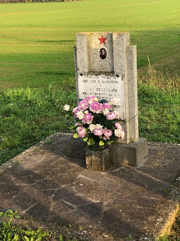 Monumento a Centolani con fiori, situato in un campo verde, in memoria di un soldato.