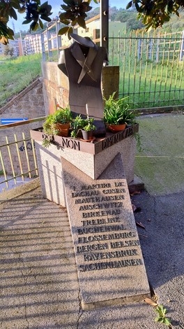 Monumento ai deportati con vestiti e piante, simbolo di memoria e commemorazione.